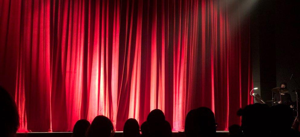 舞台灯光照亮的红色幕布，前景是观众的影子.