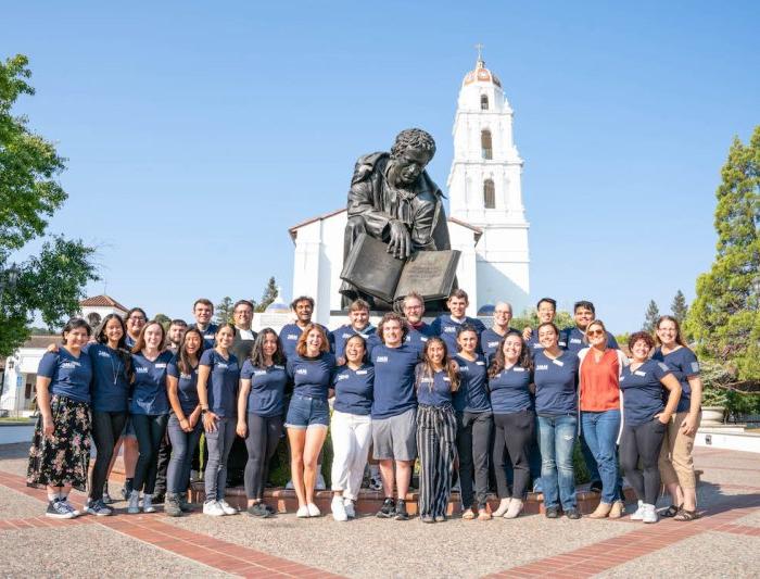 A group of Mission and Ministry workers posing in front of a chapel and a statue
